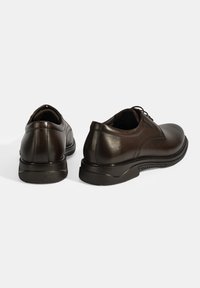 Chaussures en cuir marron avec une finition lisse, bout rond et semelle en caoutchouc basse ; comportent des lacets et un détail de couture discret sur le dessus.