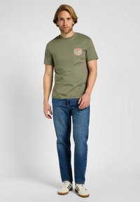 Oliwkowa bawełniana koszulka z okrągłym dekoltem i krótkimi rękawami, z czerwono-białym logo Lee Jeans na lewej piersi.