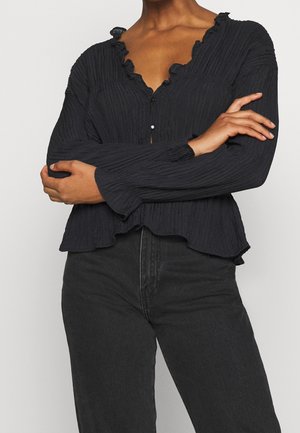 Haut noir à manches longues avec un design texturé plissé, présentant un col festonné et une fermeture à bouton avec un accent en perle.