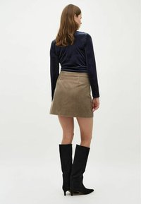 Top in velluto navy a maniche lunghe, mini gonna in corduroy color marrone chiaro e stivali neri in suede al ginocchio con punta affusolata e tacchi sottili.