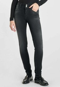 Jean skinny noir en denim avec une texture lisse, doté d'une taille haute, de deux poches frontales et d'accents en boutons argentés.