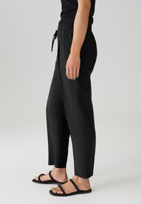 Pantalons noirs court avec une taille à cordon, fabriqués en tissu léger. Dotés de poches latérales et d'une coupe décontractée, associés à des sandales noires.