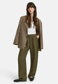 Bruin houndstooth blazer, witte tanktop, olijfgroene wijde broek en zwarte gevlochten schoenen. Casual outfit met onderscheidende textielpatronen en kleuren.