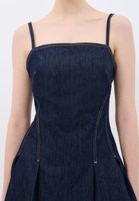 Dunkelblaue Denim-Kleid mit tailliertem Oberteil, Spaghettiträgern und detaillierten Nähten. Der Stoff hat eine glatte Textur und einen leichten Glanz.