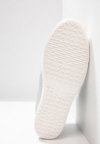 Weiße Sneaker mit einer strukturierten Gummisohle, grauem Wildleder-Obermaterial und subtilen Wellenmustern auf der Sohle. Mit Xti-Logo an der Seite.