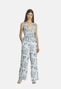 Blumiges Jumpsuit mit tiefem V-Ausschnitt, tailliertem Schnitt mit einem Peplum-Rüschensaum und weitem Bein in einem blau-weißen gemusterten Stoff.