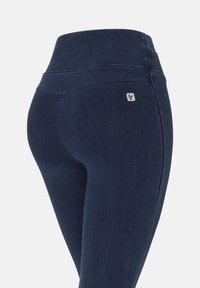 Mallas azul oscuro hechas de un material elástico similar al denim. Cintura alta con un pequeño parche de logo en la parte trasera y detalles de costura reforzada.