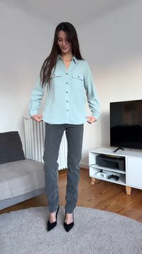 Light blue button-up shirt with two chest pockets, paired with grey jeans and black pointed heels. Smooth fabric and fitted design.