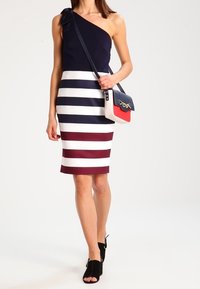 Sjömansblå klänning med en axel och breda horisontella ränder i vitt och vinrött. I kombination med en strukturerad handväska i navy, röd och vit.
