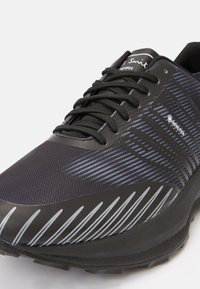 Chaussure de course noire avec une tige en mesh texturé, dotée de bandes grises réfléchissantes, de lacets et d'une semelle amortie. Détail imperméable en GORE-TEX.