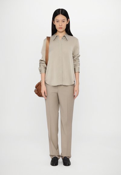 Beige long-sleeve shirt with button front, paired with beige trousers. The look is complemented by a brown shoulder bag and black shoes.