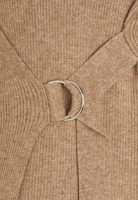 Pull en mélange de laine de couleur marron clair avec une texture côtelée et une ceinture en tissu ornée d'une boucle circulaire argentée, mettant en valeur une silhouette ajustée.
