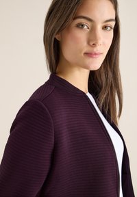 Paarse, geribbelde jas met een ritssluiting aan de voorkant en een opstaande kraag, gemaakt van gestructureerde stof. Heeft een slanke pasvorm en strakke lijnen.