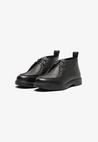 Botas de tobillo de cuero negro con un acabado texturizado, que cuentan con una punta redonda, cierre de cordones y una lengüeta para tirar en la parte trasera.