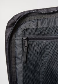 Black fabric bag with a zippered pocket featuring mesh detailing, smooth finish, and reinforced edges, highlighting durability and practicality.