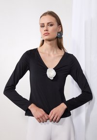 Musthave musta pikkade varruka ja V-kaelusega topp, millel on keskosas valgest kangast lill ja sile, keha järgiv tekstuur.