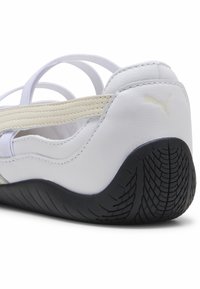 Witte sportieve schoen met elastische banden, bovenwerk van textuurleer, grijze accenten en een zwarte rubberen buitenzool met een profielpatroon.