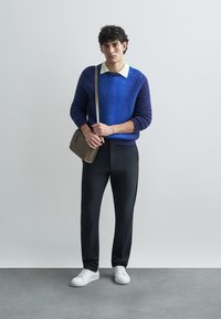 Modrý a fialový svetr s přechodem barev a límečkem s košilí pod ním, černé úzké kalhoty a bílé tenisky. Hnědá taška přes rameno.