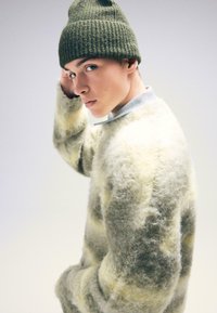 Dziany sweter w jasnoszarym kolorze z żółtymi paskami, wykonany z miękkiego, puszystego materiału. Połączony z ciemnozieloną czapką ściąganą.