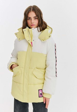Żółta i biała kurtka puchowa o teksturze sztruksu, z zapięciem na zamek błyskawiczny, dwoma kieszeniami i czarno-różową naszywką z logiem.