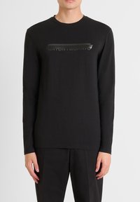 Schwarzes Langarm-T-Shirt mit einem strukturierten Druck von "ANTONY MORATO ITALIA" auf der Brust. Hergestellt aus Baumwolle, glatte Textur.