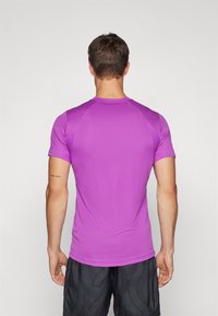 Camisa deportiva de manga corta en púrpura vibrante, fabricada con material ligero, con una textura suave y mangas raglán para un mejor movimiento.