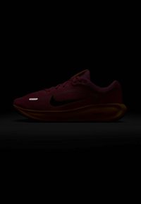 Sarkans skriešanas apavi ar teksturētu sieta augšdaļu, melna Swoosh logo, atstarojošu detaļu un dzeltenu zoli. Šņorītes ir ievietotas caur acs caurumiem.