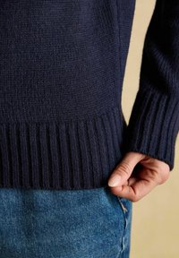 Marineblaue Strickjacke mit geripptem Saum und Bündchen, glatter Textur und figurbetontem Design, kombiniert mit hellblauen Denim-Jeans.