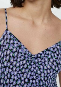 Robe florale avec une base noire, agrémentée de petites fleurs blanches et violettes. Bretelles fines et décolleté en V avec des fronces au niveau de l'encolure.