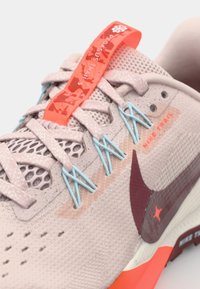 Obuv Nike Pegasus Trail 5 v svetlo béžovej farbe s vrchnou časťou z materiálu mesh, modrými a oranžovými akcentmi a štruktúrovanou podrážkou. Výrazné logo na boku.