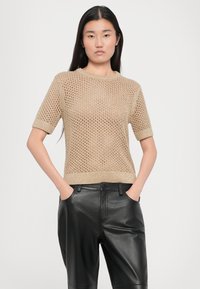 Top beige lavorato a maglia con maniche corte, caratterizzato da un design a trama aperta testurizzata, abbinato a pantaloni in pelle neri a vestibilità comoda.