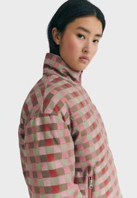 Padded checkered jacket featuring pink, red, and green squares. High collar with a zipper detail on the side, made of lightweight fabric.