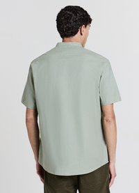 Chemise à manches courtes avec col, en tissu vert clair à texture subtile, présentant un ourlet droit et une coupe standard, vue de dos.