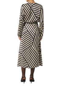 Langärmliges Kleid in Beige und Schwarz mit geometrischem Streifenmuster. Hat eine taillierte Taille und einen fließenden Rock. Getragen mit schwarzen Absätzen.