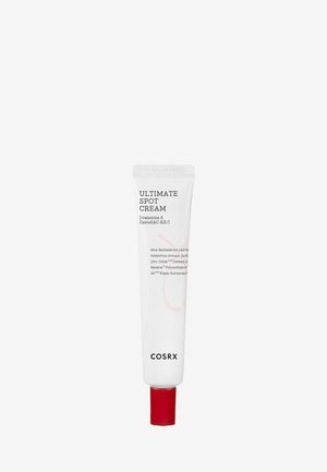 Crema para manchas Ultimate de Cosrx en un tubo blanco con tapa roja. Presenta texto claro con los ingredientes. El tubo es cilíndrico y exprimible.