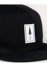 Gorra negra de tela texturizada que presenta un parche rectangular blanco con la silueta de un árbol negro y un bordado alrededor del borde.