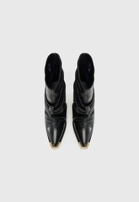 Bottes de cheville en cuir noir au design décontracté, avec des bouts pointus et un accent doré sur le capuchon. Texture lisse avec des plis doux.