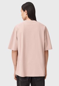 Jasnoróżowy, oversize, bawełniany t-shirt z okrągłym dekoltem, krótkimi rękawami i luźnym krojem. Prosty fason bez widocznych wzorów.