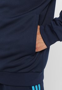 Marinblå sweatshirt med en känguruficka, ribbade ärmslut och nederkant. Texturerad tyg med ljusblå detaljer på sidorna för en sportig stil.