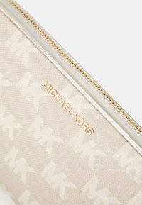Beige Michael Kors pouch with gold zipper and repeated MK logo pattern on fabric surface.