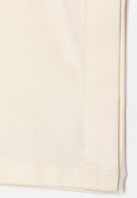 Close-up van beige stof met zichtbare zoomsteken en een omgevouwen rand.