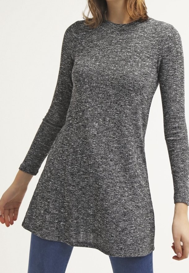 Femme portant une tunique en maille à manches longues gris foncé chiné sur un jean bleu, debout les bras légèrement écartés.