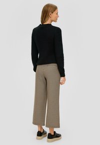 Schwarzer gerippter Strickpullover kombiniert mit braun-beigen Karottenhosen mit weitem Bein. Schwarze Sneakers mit strukturierten Sohlen runden das Outfit ab.