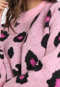 Maglione rosa con una texture morbida, caratterizzato da un motivo a stampa leopardata in nero e dettagli in rosa vivace, e un collo a girocollo a costine.