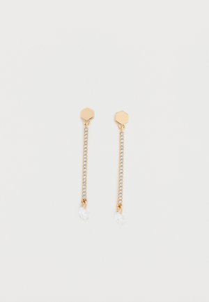 Τα σκουλαρίκια με χρυσή απόχρωση έχουν εξαγωνικό καρφί, μια σειρά από διαφανή στρας και μια στρογγυλεμένη κρεμαστή κρυστάλλινη σταγόνα στο τέλος κάθε σκουλαρικιού.