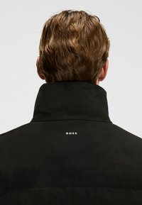 Sort, ruskindjakke med høj krave; har et lille hvidt "BOSS" logo på bagsiden. Glat tekstur og skræddersyet pasform.