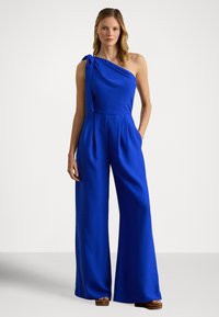 Modrý overal s jedným ramienkom vyrobený z hladkej látky; má plisované detaily v páse a široké nohavice; bez viditeľných vzorov.