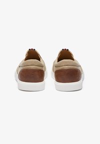 Beige stoffen sneakers met bruin leren accenten, witte rubberen zolen en een gestreept detail op de hiel. Glad textuur en een laagprofielontwerp.