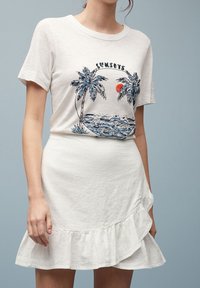 Witte T-shirt met palmboom- en zonsondergangafbeelding, gecombineerd met een witte rucheskirt. Zachte stof, casual ontwerp, aansluitende silhouet.