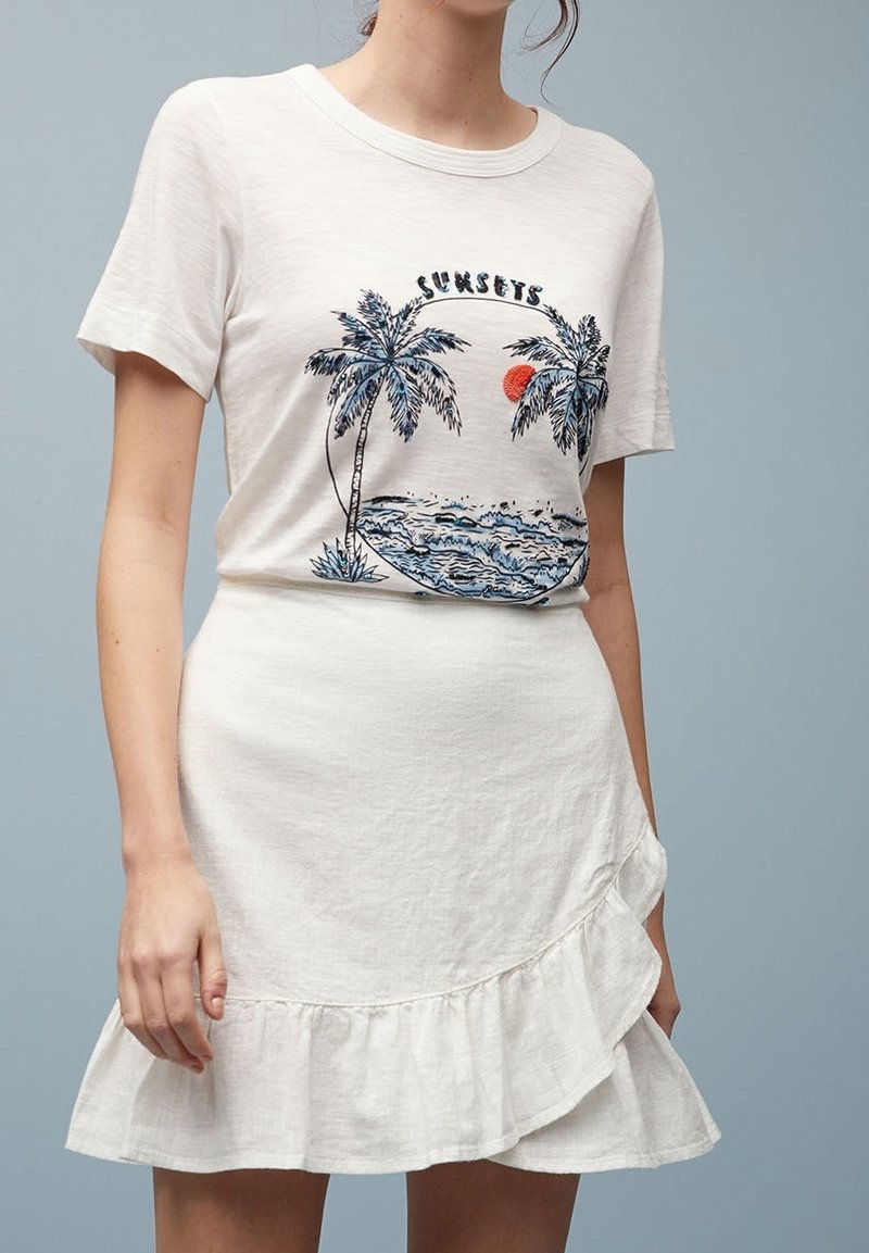 Witte T-shirt met palmboom- en zonsondergangafbeelding, gecombineerd met een witte rucheskirt. Zachte stof, casual ontwerp, aansluitende silhouet.